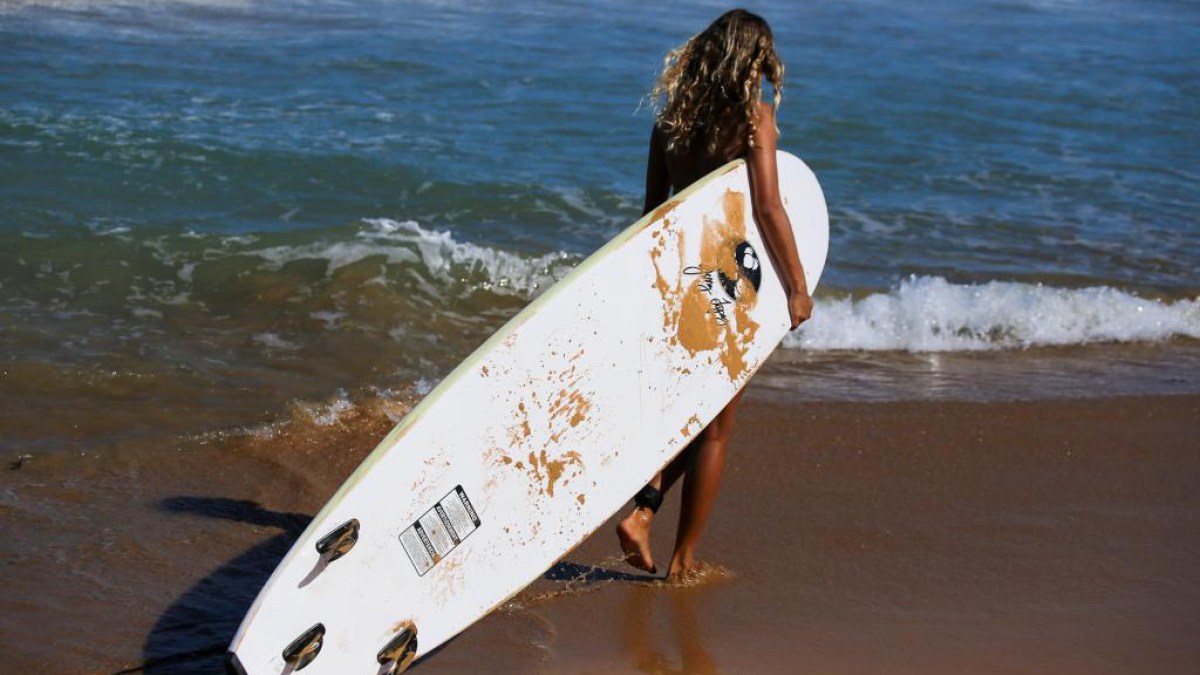a person in a wet suit standing on a beach holding a surf board