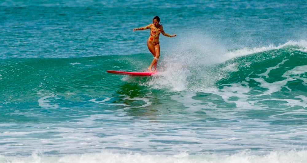 Surfer riding a wave on a red surfboard in the ocean, wearing a floral swimsuit.